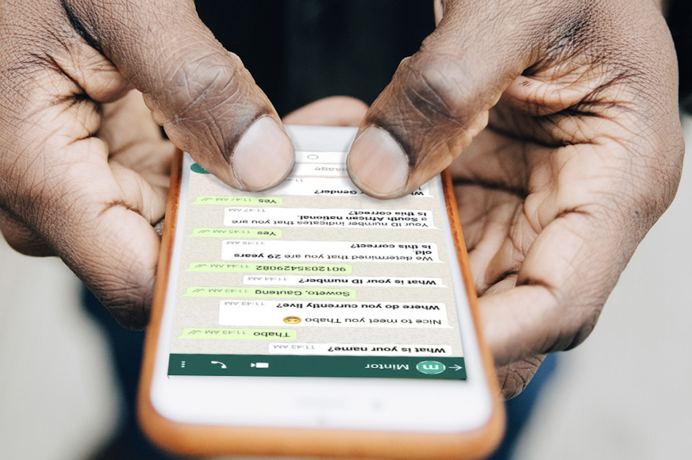 Close-up of a person of color using a smartphone to answer identity verification questions in a mobile chat interface.