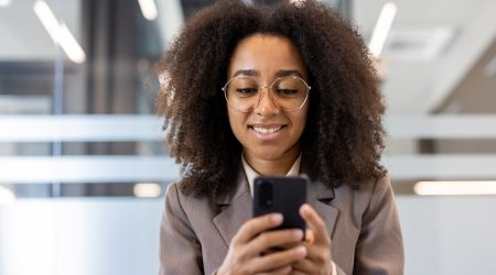 A smiling HR professional in an office using a smartphone to manage employee engagement and automation.