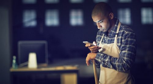 Shot of a young man working late on a cellphone in his coffee shop.